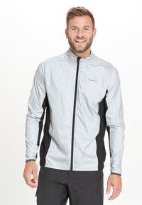 Letvægts, sølvfarvet vindjakke med sorte sidepaneler, høj krave og fuld lynlås. Har lange ærmer og et sporty design.