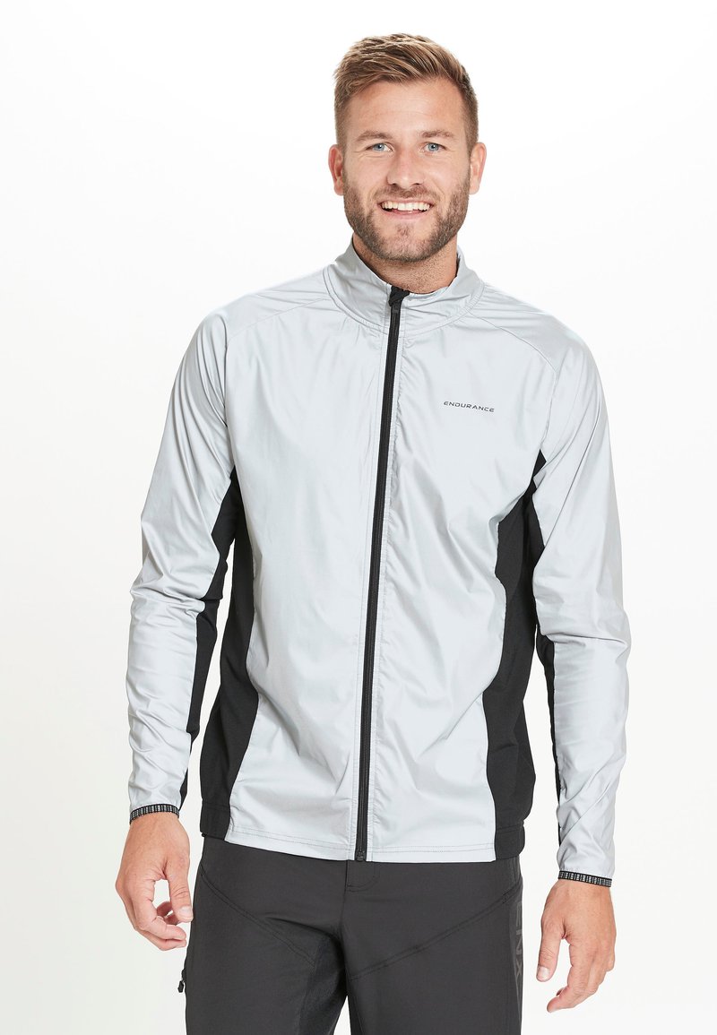 Letvægts, sølvfarvet vindjakke med sorte sidepaneler, høj krave og fuld lynlås. Har lange ærmer og et sporty design.