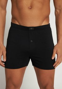 Zwarte katoenen boxershorts met een elastische tailleband, met een sluiting met een knoop aan de voorkant en een klein merklabel op de taille.