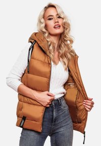 Gilet matelassé marron avec capuche, fermeture zippée, poignets à côtes et étiquette extérieure. L'intérieur présente une doublure pour la chaleur et le style.
