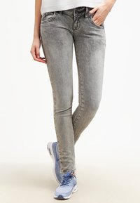 Jean skinny gris clair avec une finition délavée, design à cinq poches et passants de ceinture, associés à des chaussures de sport bleues et blanches.
