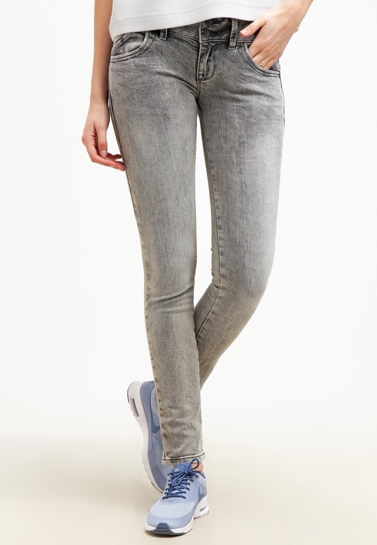 Jean skinny gris clair avec une finition délavée, design à cinq poches et passants de ceinture, associés à des chaussures de sport bleues et blanches.