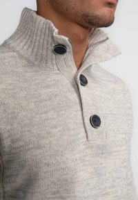 Maglione lavorato a maglia grigio chiaro con colletto alto, caratterizzato da tre bottoni neri e un motivo testurizzato. Tessuto morbido con dettaglio a costine.