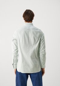 Camicia a maniche lunghe verde chiaro con un motivo testurizzato, polsini con bottoni e orlo arrotondato. Realizzata in un tessuto liscio e leggero.