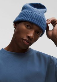 Kék kötött sapka bordázott textúrával, világosabb kék díszcsíkkal. Egy személy viseli, aki szintén kék pólót hord.