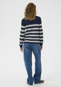 Tumed ja valged triibulised kampsun ribakujulise tekstuuriga, pikad varrukad ja mugav lõige, koos laia jala siniste denimpükstega.