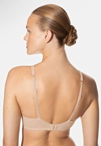 Soutien-gorge en dentelle beige avec des bretelles réglables, doté de bords festonnés et d'une fermeture à crochet et œillet. Tissu lisse et motif délicat visibles.