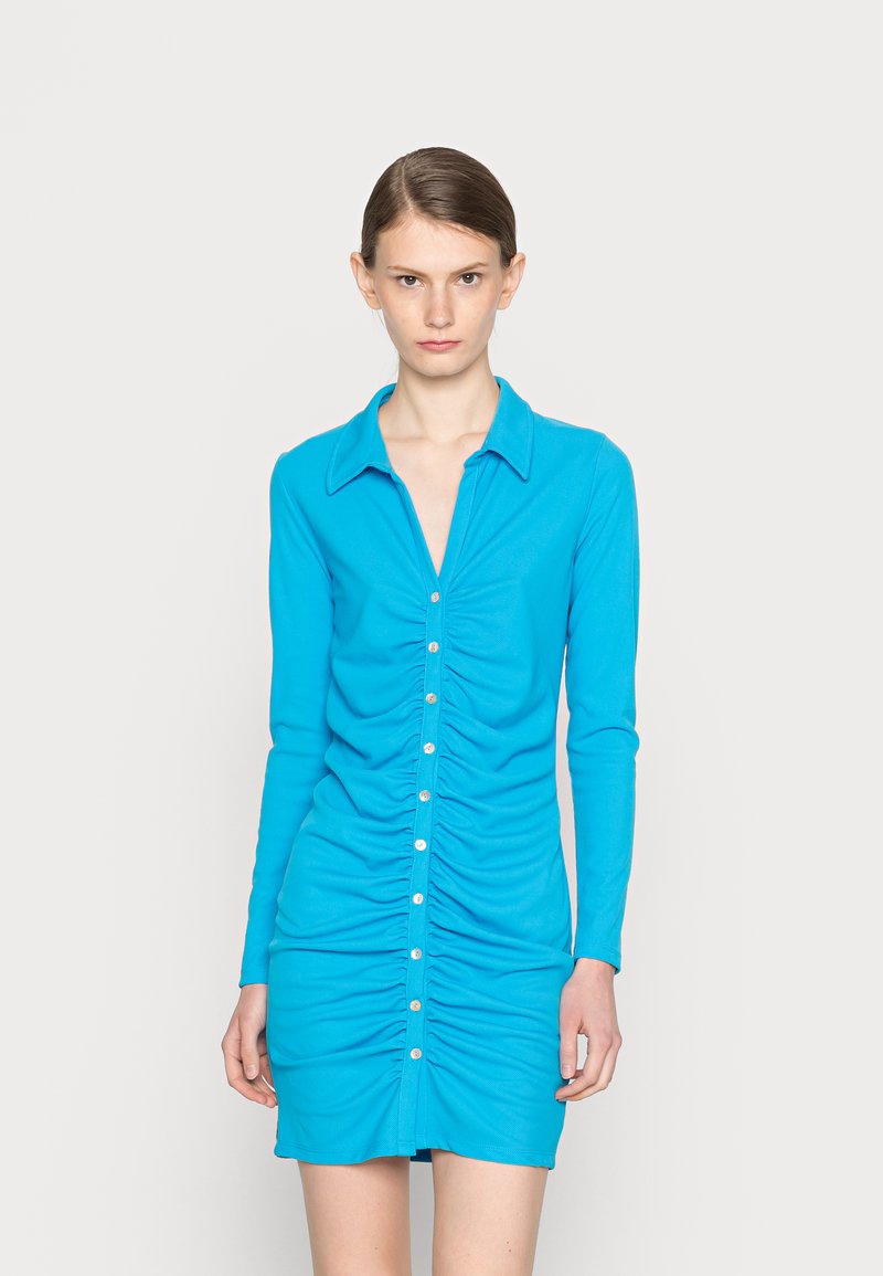 Vestido justo de mangas longas em azul brilhante, com fechamento frontal por botões, lados franzidos e gola. Tecido suave e elástico com um design elegante.