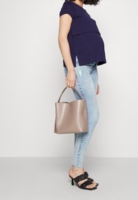 Top de manga corta de color azul marino con diseño en capas, jeans ajustados desgastados de color azul claro, sandalias negras con volantes y un bolso liso de color topo.