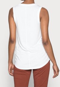 Top bianco senza maniche con orlo arrotondato, texture morbida e cucitura posteriore dritta. Abbinato a pantaloni marroni, che presentano una silhouette con vestibilità rilassata.