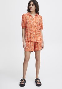Orange floral print two-piece outfit featuring a button-up short-sleeve top and coordinating shorts, both with a relaxed fit and soft fabric.