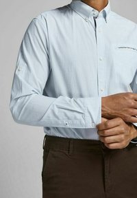 Světle modrá pruhovaná košile na knoflíky s límečkem, dlouhými rukávy a kapsou na prsou. Bavlněná tkanina s hladkým povrchem a jemnými detaily.