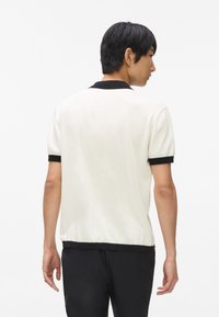 Rövid ujjú pólókrém színben, fekete gallérral és mandzsettákkal. Puha tapintás, testhezálló fazon és letisztult vonalak modern sziluettet alkotnak.
