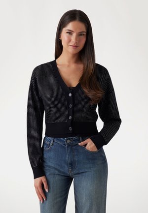 Cardigan negru scurt cu decolteu în V, decorat cu puncte mici albe și finisat cu nasturi închiși. Purtați peste un top asortat și jeansi din denim.
