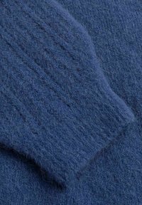 Blauwe wollen kleding heeft een zachte, gestructureerde brei, met ribbels langs de mouw. Close-up benadrukt het gezellige, fuzzy uiterlijk.