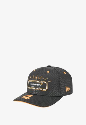 Schwarze Kappe mit einem komplexen geometrischen Muster, orangefarbenen Akzenten und einem weißen Logo-Aufnäher der McLaren Formel 1 Mannschaft auf der Vorderseite.