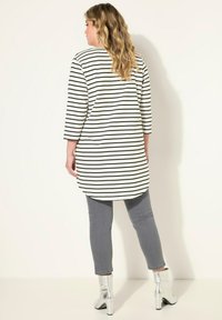 Schwarz-weißer gestreifter langer Tunika-Oberteil mit Dreiviertelärmeln, kombiniert mit grauen Skinny-Jeans und glänzenden silbernen Ankle Boots.
