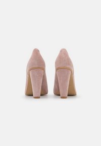 Rosa mockaskor med hög klack, spetsig tå, tjock blockklack och slät textur. Kanter och klack har en kontrasterande ljusbrun kant.