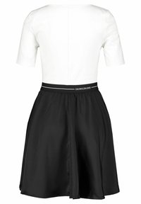 Vit kortärmad topp med svart utsvängd kjol fäst, elastiskt midjeband med "Calvin Klein Jeans"-branding, bakvy.