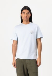 T-shirt en coton bleu clair à manches courtes, col rond, avec un logo en triangle sur la poitrine gauche arborant des accents multicolores.