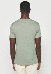 Trumpas rankovėmis, apvalia iškirpte marškinėliai, pagaminti iš minkštos medžiagos, su laisvu siluetu ir minimalizmo stiliumi, muted green spalvos.