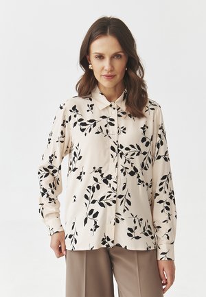 Cream blouse with black leaf pattern, button-up front, and long sleeves. Smooth fabric with a classic collar and straight hem.
