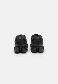 Black athletic shoes with a mesh upper, padded collar, and a textured rubber sole. Features a glossy blue accent across the midsole.
