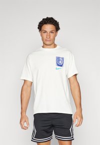 White cotton t-shirt with a blue graphic pocket and a turquoise Nike logo. Short sleeves and a round neckline. Black mesh shorts with white accents.