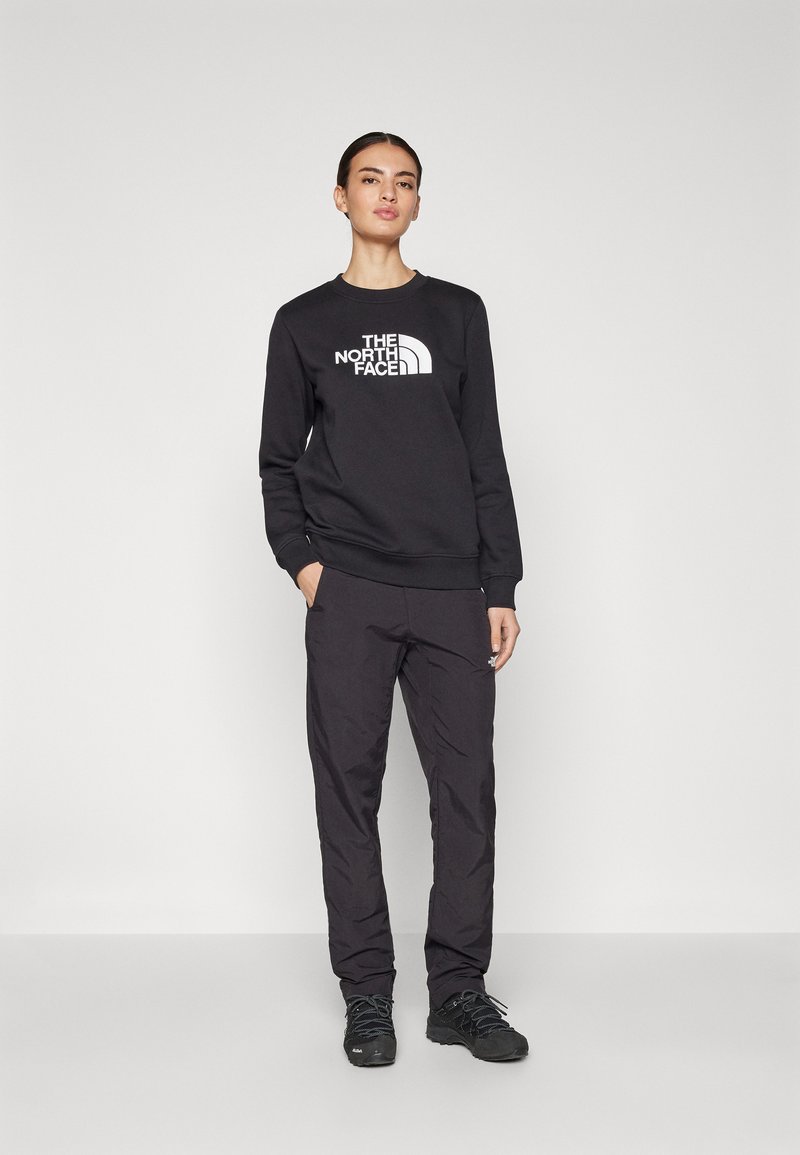 Zwarte sweatshirt met wit "The North Face" logo, gecombineerd met zwarte broeken met een relaxte pasvorm en verschillende texturen, gedragen met zwarte schoenen.