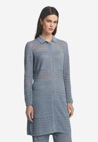 Ljusblå lång cardigan med knappstängning på framsidan, med intrikata öppna stickmönster och krage. Mjuk textur, slim fit.