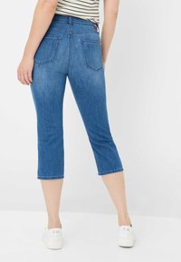 Jeans capri in denim blu con un design aderente, vita media e due tasche posteriori. Si fermano poco sotto il polpaccio con un orlo arrotolato.