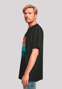 Zwarte t-shirt met korte mouwen met een kleurrijke bergafbeelding in tinten van oranje, blauw en groen op de voorkant. Relaxte pasvorm.