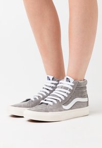 Wysokie sneakersy wykonane z szarego zamszu z białymi akcentami, posiadające sześć przelotek, płaskie białe sznurówki oraz teksturowany kołnierz.