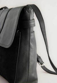 Sac à main en cuir noir avec une surface texturée, fermeture à rabat plate, bandoulière ajustable et détails de couture subtils.
