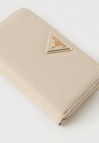 Bézs színű, texturált pénztárca arany háromszög alakú logó táblával, cipzáras záródással és sima élekkel. A texturált felület vizuális érdeklődést kelt.
