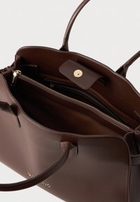 Brūna ādas rokassoma ar gludu tekstūru, zelta furnitūru un divām iekšējām rāvējslēdzēju nodalījumam. Aprīkota ar divām rokturiem un sprādzes aizdari.