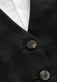 Must mustriga v-kaelusega must vest, kaunistatud kahe ümmarguse marmorist nööbiga. All on nähtav valge triibuline särk. Sile tekstuur.