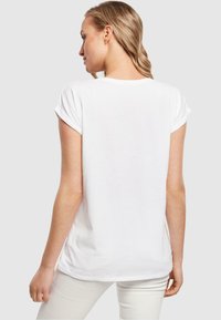 Weißes T-Shirt mit kurzen, aufgeknöpften Ärmeln, aus weichem Baumwollstoff, abgerundetem Saum und lässiger Passform, von hinten gezeigt.