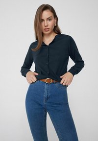 Camisa de botones color navy con mangas largas y cuello, combinada con jeans azul de cintura alta y un cinturón marrón con una hebilla cuadrada.