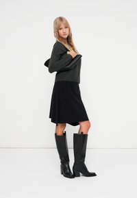 Svarte læderknæhøje støvler med blokhæle, parret med en mørk nederdel og grå sweater. Glat tekstur og strømlinet design.