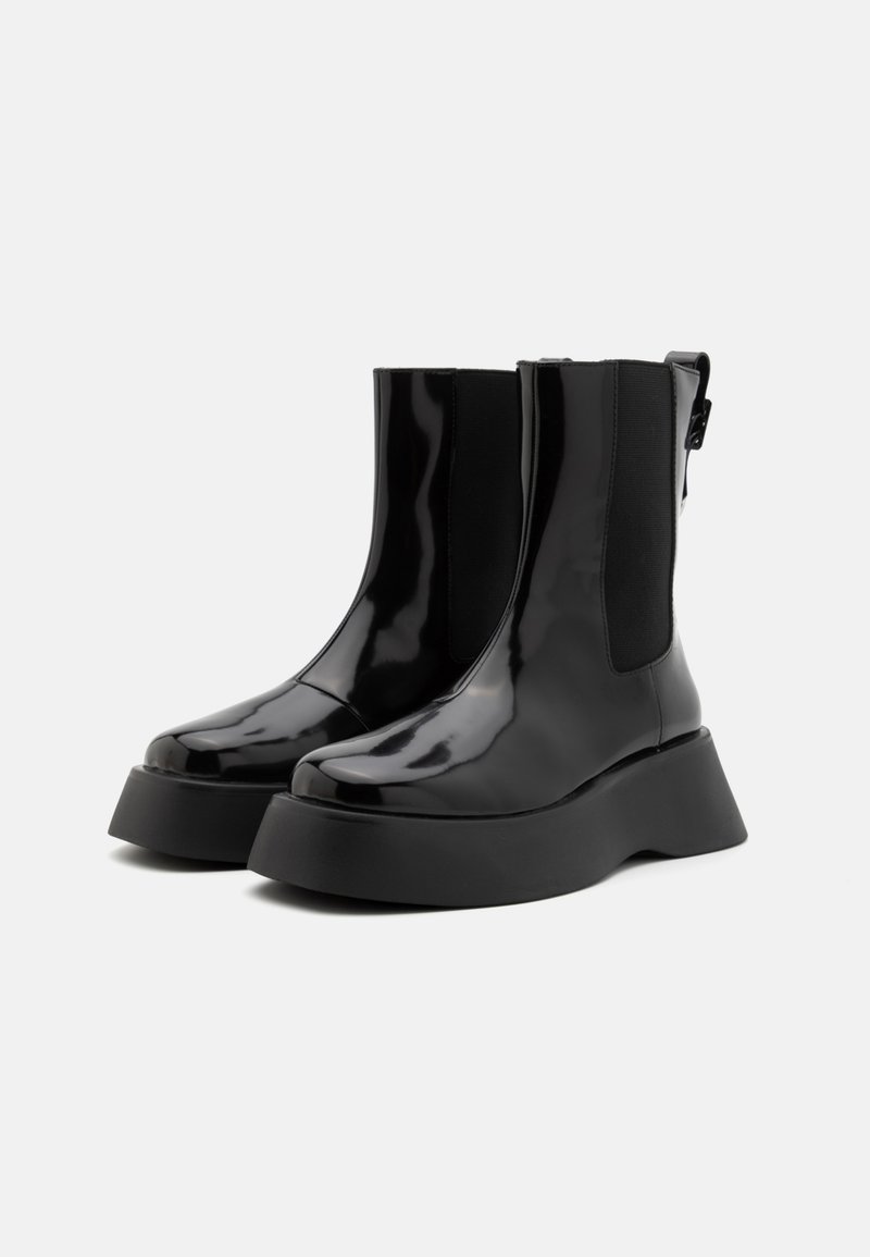 Czarne lakierowane botki za kostkę z masywną czarną podeszwą platformową, z elastycznymi panelami bocznymi i tylną pętelką dla łatwego zakładania.
