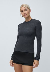 Ribbed pitkähihaine paita tummanharmaana, jossa on pyöreä kaula-aukko ja tiukka siluetti. Yhdistetty mustiin shortseihin.