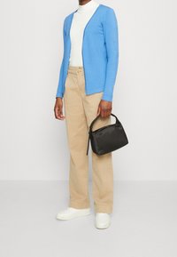 Blå lätt cardigan, vit polotröja, beige vida byxor och svart handväska. Vita sneakers fulländar outfiten.