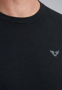 Zwarte, gebreide trui met een ronde hals, voorzien van een structuurstof en een klein, geborduurd logo van vleugels op de linkerborst.