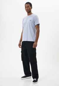 Camiseta de algodón de color púrpura claro con mangas cortas y un pequeño gráfico en el pecho, combinada con pantalones cargo negros y zapatillas negras.