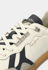 Baskets Pepe Jeans London blanches et bleu marine avec des détails beige et des lacets blancs sur fond clair.