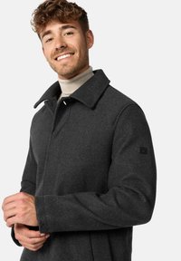Gray wool coat with a wide collar, front snap closure, long sleeves, and a textured finish. Features a logo detail on the sleeve.