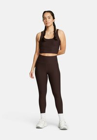 Top sportivo a coste marrone e leggings a vita alta coordinati. Realizzati in tessuto elastico con una superficie liscia. Sneakers bianche con accenti.