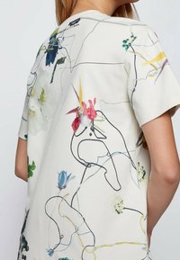 Kortärmad krämfärgad t-shirt med blommönster i olika färger, omdrawn i svart, med en avslappnad passform och mjuk textur.