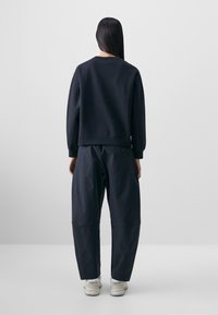 Dark navy sweatshirt with dropped shoulders paired with loose-fit trousers. Smooth fabric with a subtle sheen, elastic cuffs, and waistband.